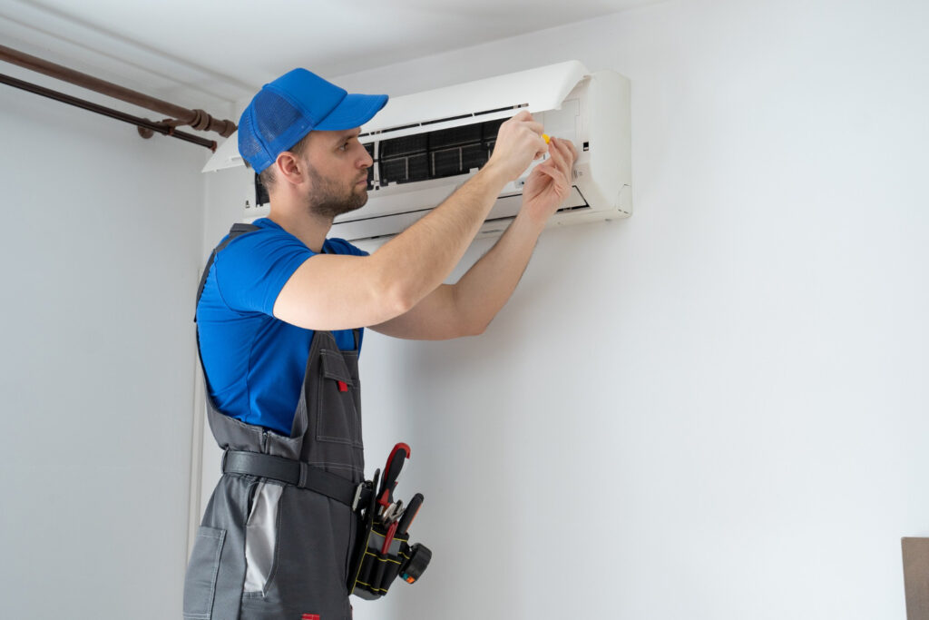 HVAC technician performing maintenance on a wall-mounted air conditioning unit in a residential setting, illustrating home cooling solutions relevant to HVAC services in Corsicana.